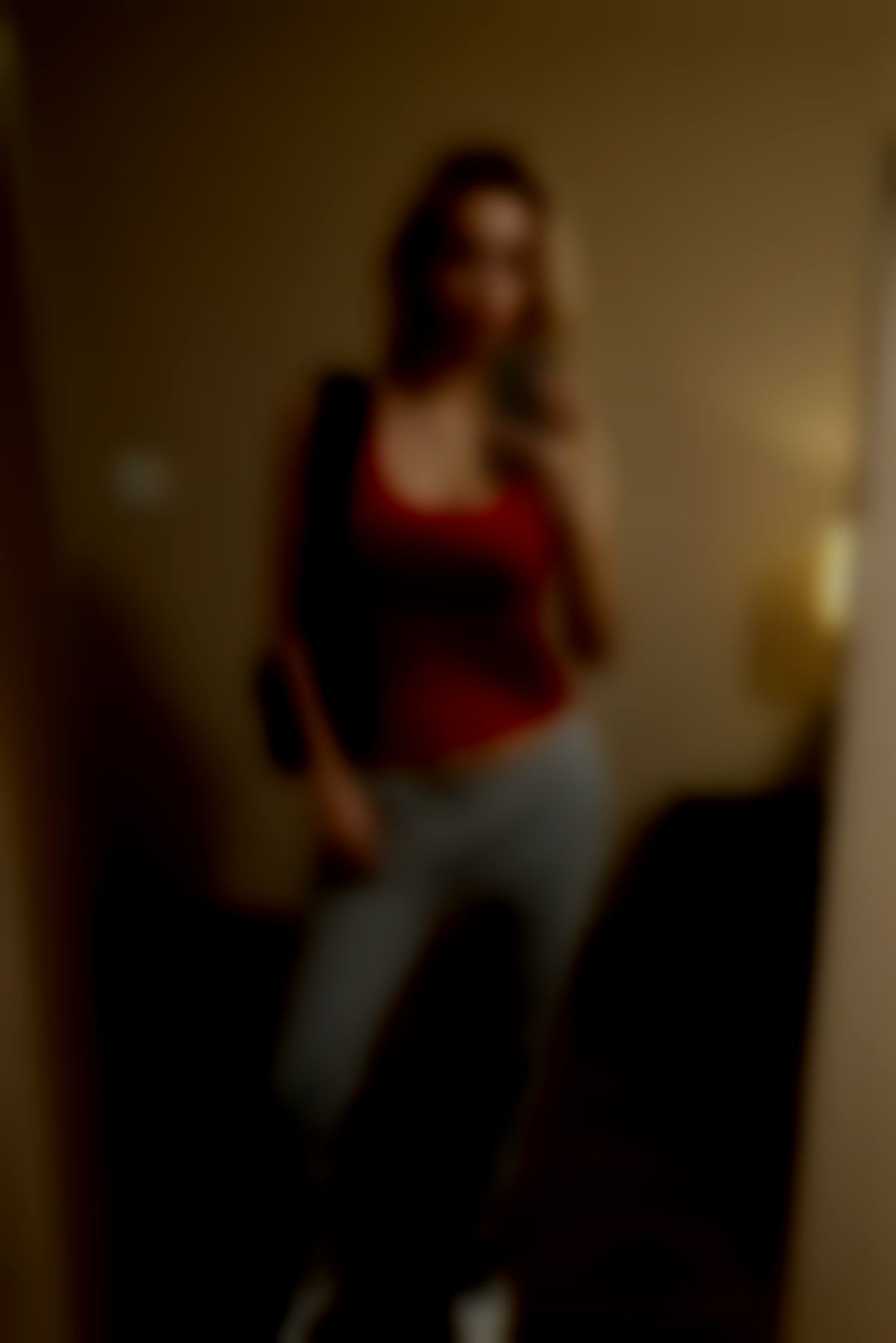 Slim blonde standing in front of mirror gripping phone in her right hand.