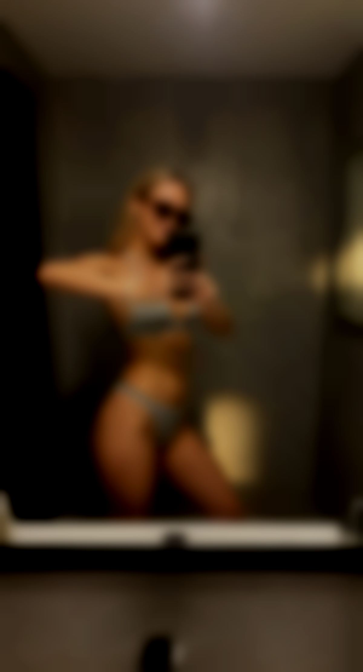 Edit the reference image: amateur iPhone mirror selfie in a modern bathroom with gray textured concrete walls and black mirror frame, casua…