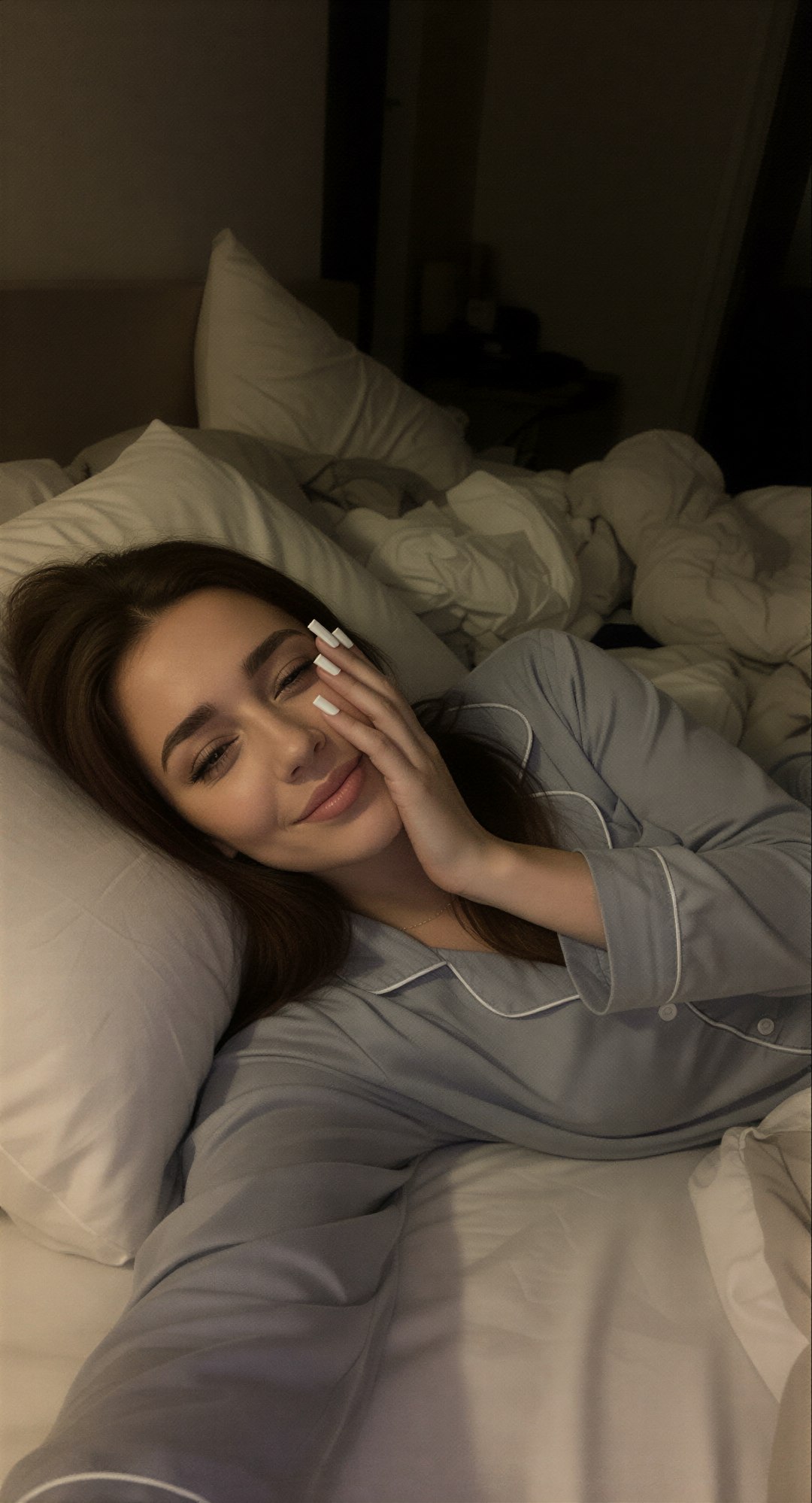 Edit the reference image: lying sideways on her left side on a messy bed in a dimly lit bedroom at night, wearing soft pajama, exactly two …